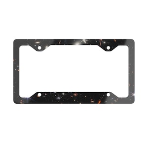 May include: License plate frame with a black background featuring a vibrant image of a galaxy filled with stars and celestial bodies. The frame has a rectangular shape with four mounting holes.