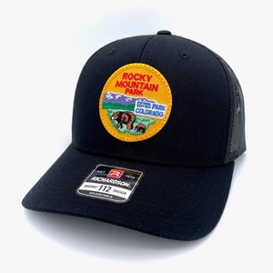 May include: Black trucker hat with a yellow patch featuring a bear and the text "Rocky Mountain Park Estes Park Colorado". The hat is made by Richardson 112.