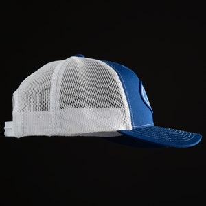 May include: A royal blue and white trucker hat with a white mesh back and a blue front. The hat has a white circle with a blue outline on the front.