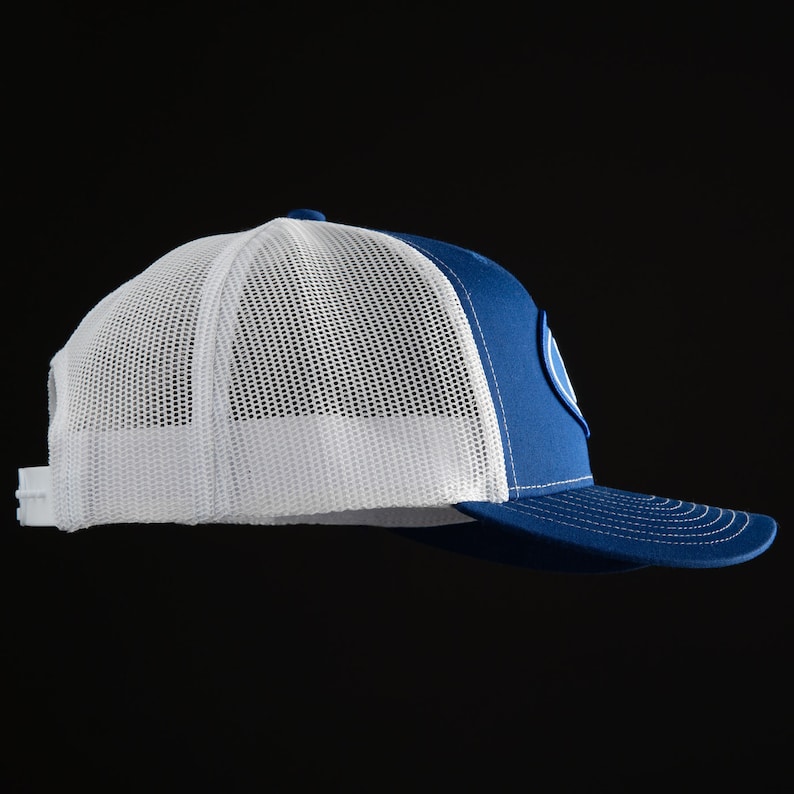 May include: A royal blue and white trucker hat with a white mesh back and a blue front. The hat has a white circle with a blue outline on the front.