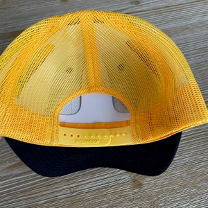May include: Yellow and black mesh trucker hat with an adjustable strap and the word "RICHARDSON" printed on the strap.