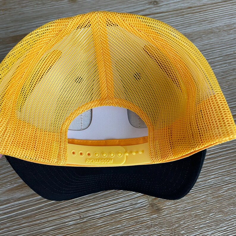 May include: Yellow and black mesh trucker hat with an adjustable strap and the word "RICHARDSON" printed on the strap.