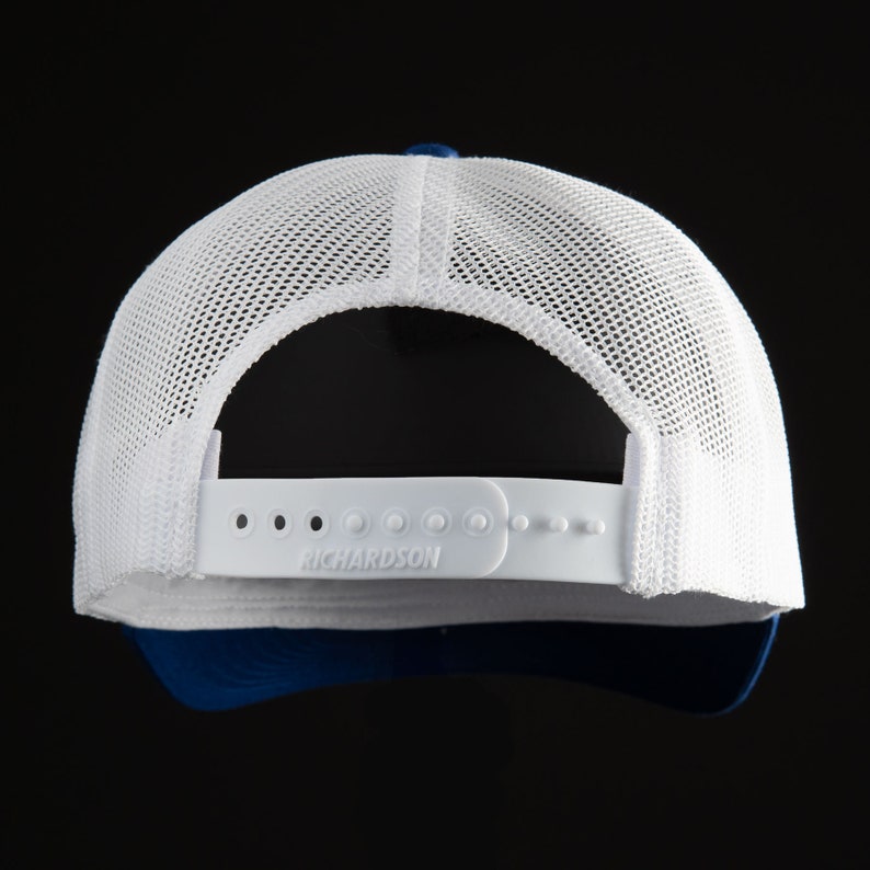 May include: White and blue trucker hat with a mesh back. The hat has a white adjustable strap with the word "RICHARDSON" printed on it.