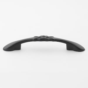 May include: A black cabinet pull with a curved design. The handle features a floral pattern in the center and is made of a solid, matte black material. The pull is designed for easy gripping and opening of drawers or cabinets.