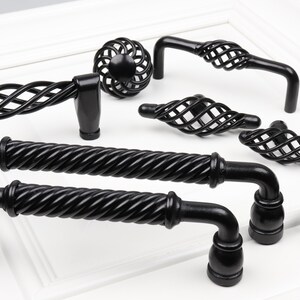 May include: A set of eight black metal cabinet knobs and pulls with a variety of styles, including twisted rope, cage, and T-shaped designs.