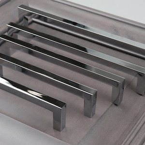 May include: Five silver cabinet pulls with a rectangular shape and a square end. The pulls are arranged in a row, with the largest pull at the top and the smallest pull at the bottom.