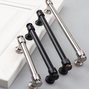 May include: Four cabinet pulls, two in black and two in silver, with a vintage style. The pulls have a rounded, slightly curved design with a small knob at the end.