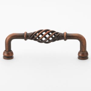 May include: A copper-toned cabinet pull with a twisted, woven design. The pull has a rounded, slightly curved shape.