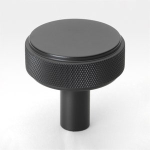 May include: Black metal knob with a round top and a textured, knurled base. The knob has a cylindrical stem.