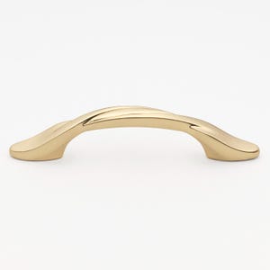 May include: A gold-toned cabinet pull with a twisted design. The pull has a smooth, rounded shape and a polished finish.