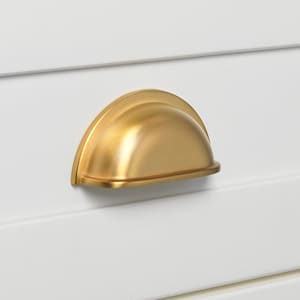 May include: A gold-toned cabinet pull with a rounded, arched shape. The pull is mounted on a white surface.
