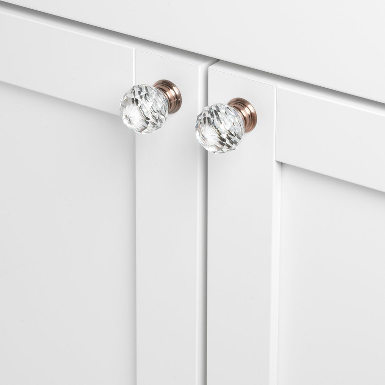 May include: Two clear crystal cabinet knobs with a faceted design and a copper finish.