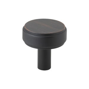 May include: A black cabinet knob with a round, slightly raised top in an oil rubbed bronze finish. The knob has a cylindrical stem.
