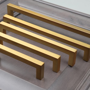 May include: Five gold cabinet pulls of varying lengths, arranged in a row from shortest to longest.