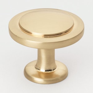 May include: A brushed gold cabinet knob with a round, raised center and a smaller, round base.