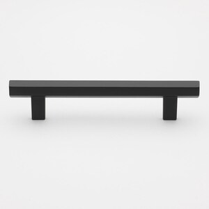 May include: Black cabinet hardware pull with a square shape and a flat, rectangular design.