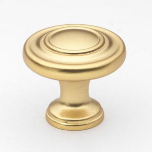 May include: A gold cabinet knob with a round, slightly raised top and a smooth, rounded base.