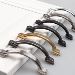May include: Five different cabinet pulls in various finishes, including brushed nickel, oil rubbed bronze, polished brass, and satin nickel. The pulls are all the same shape, with a curved arch and square ends.