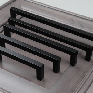May include: Five black metal cabinet pulls of varying lengths. The pulls have a rectangular shape with rounded corners.