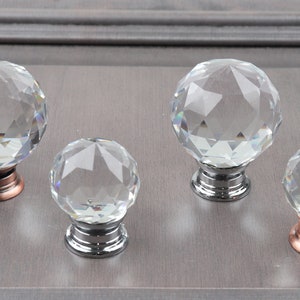 May include: Four crystal cabinet knobs with faceted surfaces. The knobs have a silver or copper base.