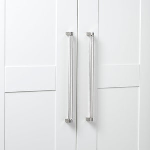 May include: White cabinet doors with two long, clear acrylic and brushed nickel cabinet pulls. The pulls are vertically aligned and centered on the doors. The cabinet doors have a recessed panel design.