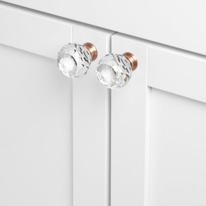 May include: Two clear crystal cabinet knobs with a faceted design and a copper finish.