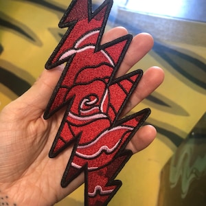 May include: Red embroidered patch with a lightning bolt design and a rose inside. The rose is outlined in white.