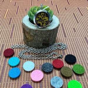 May include: A silver aromatherapy necklace with a circular pendant featuring a yellow and black floral design. The necklace is displayed with a silver chain and several colorful felt pads. The pendant is approximately 1 inch in diameter.