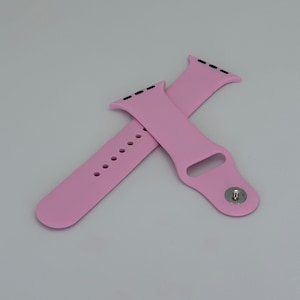 May include: Two light pink watch bands. One band has a series of holes for adjustment, and the other has a metal clasp. Both bands have black lines at the top where they attach to the watch face. The bands are made of a flexible material.