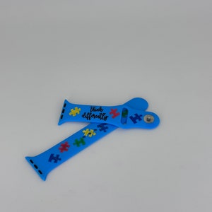May include: A light blue watch band with a puzzle piece design and the words "Think Differently" in black and red. The band features colorful puzzle pieces in yellow, red, green, and blue.