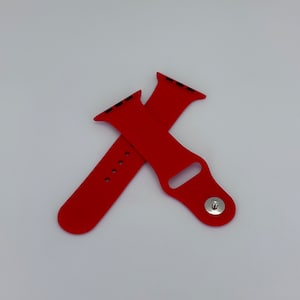 May include: Two bright red watch bands are displayed against a white background. One band is positioned over the other, showing the pin and the holes for the watch. The bands are made of a smooth, flexible material.