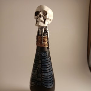 May include: A black glass bottle with a white skull and silver dripping wax on the top. The bottle has a blue and white ribcage design and the text "You Can't Stop Me" on the bottom.