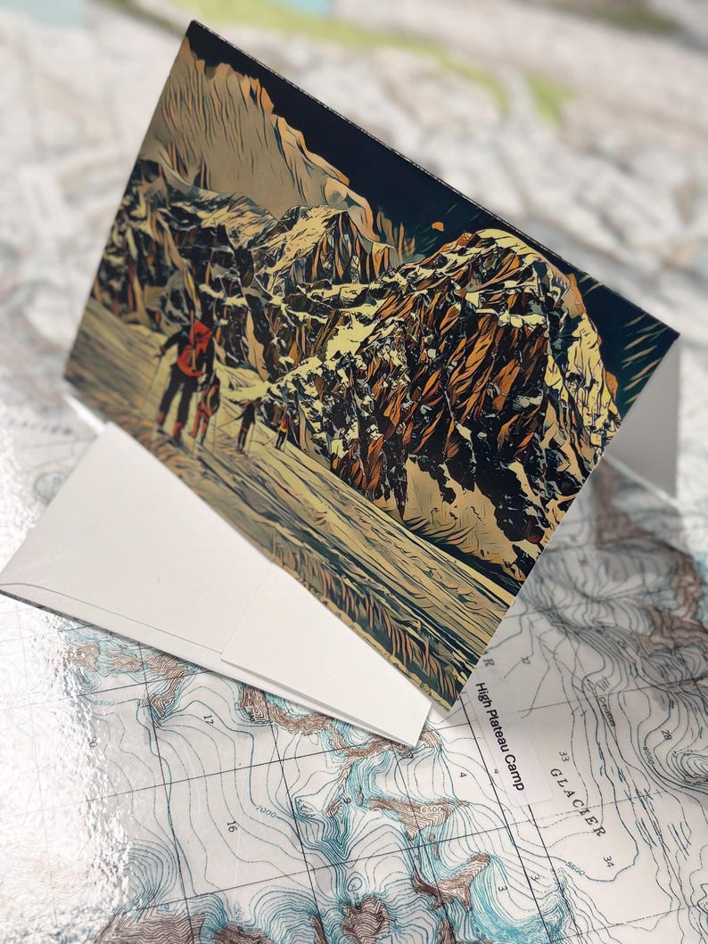 Puede incluir: Una tarjeta de felicitaci&oacute;n plegada con un paisaje monta&ntilde;oso estilizado con figuras, probablemente excursionistas. La tarjeta es blanca, con la imagen en tonos marrones, beige y azules. Descansa sobre un mapa topogr&aacute;fico detallado.