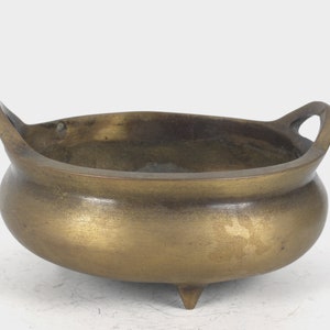 May include: A gold-colored metal incense burner with two handles and three legs. The burner has a rounded shape and a smooth surface.