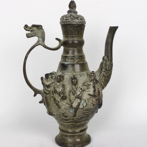 Puede incluir: Una tetera de bronce verde con un asa de dragón y una tapa con detalles intrincados. La tetera está decorada con figuras en relieve de personas y un dragón.