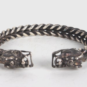 May include: Silver bracelet with a twisted rope design and dragon head ends.