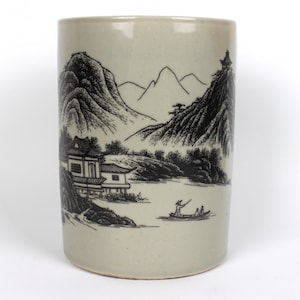 Puede incluir: Una taza de cerámica con un diseño de paisaje en blanco y negro. El diseño presenta montañas, un río, una casa y un barco con personas en él.