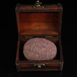 May include: A small wooden treasure chest with a hinged lid is open, revealing a round, iridescent, multi-coloured stone inside.