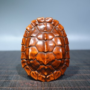 Puede incluir: Una escultura de caparazón de tortuga de madera tallada con un rico color marrón. El caparazón está intrincadamente detallado con escamas individuales.