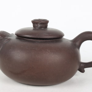 May include: A brown ceramic teapot with a lid shaped like a pig's head. The teapot has a rounded body and a curved handle.