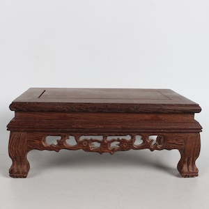 May include: A dark brown wooden table with intricate carvings on the bottom edge. The table has a rectangular top and four legs.