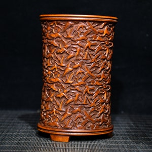 Peut inclure: Un vase en bois cylindrique avec un motif sculpté d'oiseaux en vol. Le vase est de couleur brun foncé et a une finition lisse. La base du vase est légèrement évasée.