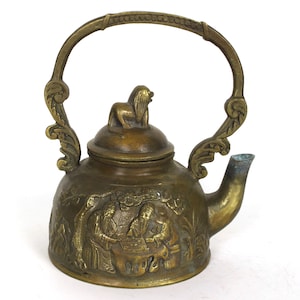 May include: A small, ornate brass teapot with a lion finial on the lid. The teapot has a detailed design of figures and foliage.