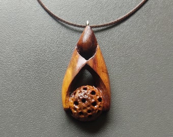 May include: A wooden pendant necklace with a carved, intricate design. The pendant features a round, textured sphere in the center.