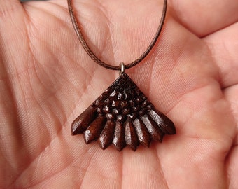 May include: A brown wooden pendant necklace with a fan-shaped design. The pendant is intricately carved with a geometric pattern.