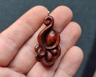 May include: A dark brown wooden pendant with a swirling, organic design. The pendant has a silver loop at the top for attaching to a chain.