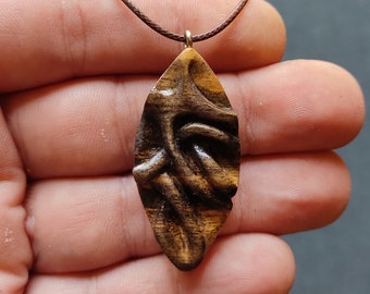 May include: A wooden pendant necklace with a dark brown and light brown wood grain pattern. The pendant is shaped like a teardrop and has a carved design.