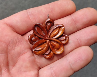 May include: A wooden pendant carved in the shape of a flower with five petals. The pendant is a deep reddish-brown color and has a smooth, polished finish.