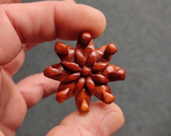 May include: A hand-carved wooden flower with a six-pointed star shape and a detailed design. The flower is a deep reddish-brown color and has a glossy finish.