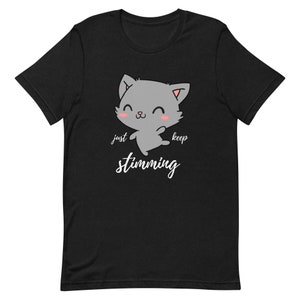 Op de afbeelding: Zwart T-shirt met een cartoon grijze kat met roze wangen en de tekst "just keep stimming" in wit.